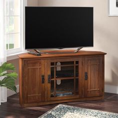 a large flat screen tv sitting on top of a wooden entertainment center next to a window