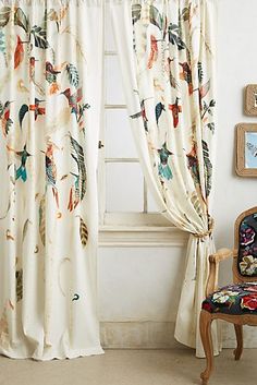 the curtains in this room are decorated with colorful flowers and feathers, while the chair is next to it