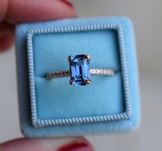 someone is holding an engagement ring that has a blue stone in the middle and diamond band around it