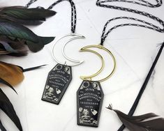 Add a touch of spooky playfulness with this Moon Coffin Necklace. Featuring a long black figaro chain that holds a gold crescent moon and a resin coffin that has a Ouija board printed on both sides. This is the perfect mix of witchy and magical. NECKLACE LENGTH: 32inches (Approx 81cm) MATERIAL: Brass Coated Iron Chain, Gold Plated Alloy Moon, Resin Coffin Pendant COLOR: Black and Gold QUANTITY: 1 Necklace For more HALLOWEEN designs, CLICK HERE! https://www.etsy.com/shop/SpotLightJewelry?ref=seller-platform-mcnav&search_query=Halloween For more GOTHIC designs, CLICK HERE! https://www.etsy.com/shop/SpotLightJewelry?ref=seller-platform-mcnav&search_query=Gothic THANK YOU FOR CHOOSING SPOTLIGHT JEWELRY! Our mission is to put a SpotLight on Women and their unlimited potential. At Spotlight Jewe Halloween Moon Charm Jewelry As Gift, Mystical Black Necklace For Halloween, Black Halloween Jewelry With Charms, Halloween Black Jewelry With Charms, Witchy Gold Jewelry For Halloween, Black Moon Charm Jewelry For Halloween, Black Halloween Moon Charm Jewelry, Spooky Black Necklace For Gift, Black Mystical Jewelry For Halloween