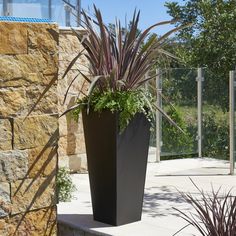 a tall black planter sitting on top of a cement slab next to a stone wall