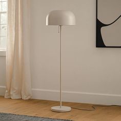 a white floor lamp sitting on top of a hard wood floor next to a window