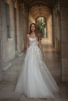 a woman in a white wedding dress standing on a stone walkway with an archway behind her