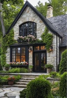 a stone house with black windows and lots of greenery on the front door, steps leading up to it