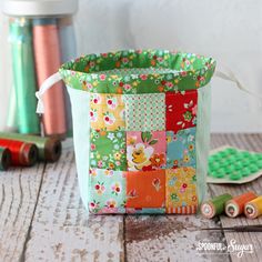 a patchwork basket sitting on top of a wooden table next to thread and spools