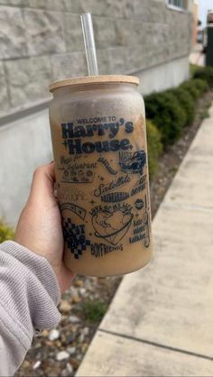 a person holding up a drink in front of a building with the words harry's house written on it