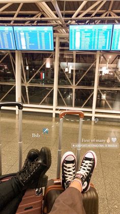 a person's feet resting on luggage in an airport with two signs above them