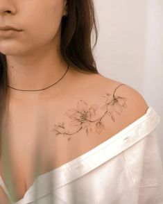 a woman wearing a white shirt has a flower tattoo on her left shoulder and chest