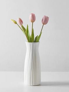 three pink tulips in a white vase on a table with light grey background