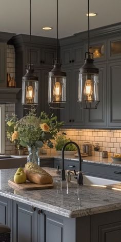 a kitchen with gray cabinets and marble counter tops, hanging lights over the island area