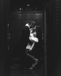 black and white photograph of a couple kissing in an elevator with their arms around each other