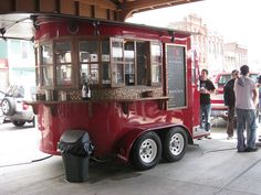 a red food truck parked in a parking lot with people standing around and looking at it