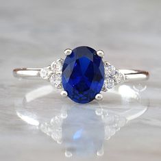 ♥ Beautifully handcrafted Blue Sapphire ring that features 1.5-carat classic oval cut Sapphire gemstone with brilliant-cut Diamond accents (5A grade CZ) in solid Sterling Silver. ♥ This ring makes the perfect engagement or anniversary gift for her that will be treasured forever! ♥ Blue Sapphire is traditionally associated with love and purity. It's said to bring prosperity and attract gifts of all kinds. Metal: Solid 925 Sterling Silver Gemstone: Blue Sapphire Side Stones: Diamond simulants (5A Silver Oval Rings With Side Stones, Oval Silver Rings With Side Stones, Classic Blue Cubic Zirconia Birthstone Ring, Oval Rings With Side Stones For Anniversary, Oval Jewelry With Side Stones For Gift, Oval Diamond Ring With Side Stones For Promise, Oval Diamond Promise Ring With Side Stones, Gift Oval Jewelry With Side Stones, White Gold Oval Rings With Side Stones