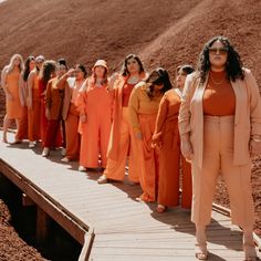 a group of women in orange outfits standing on a wooden walkway with one woman looking at the camera