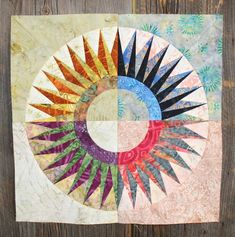 a circular quilt on a wooden surface with many different colors and shapes in the center