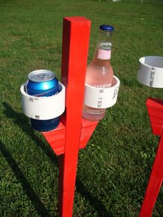 there is a red pole with two water bottles on it and a cup holder in the grass