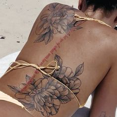 a woman with tattoos on her back sitting in the sand