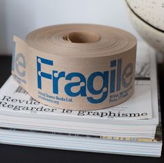 there is a roll of fragile tape on top of some magazines next to a bowl