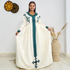 a woman standing in front of a wall wearing a white dress with green trims