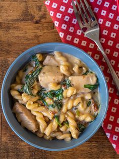 a blue bowl filled with pasta and spinach next to a red napkin on top of a wooden table