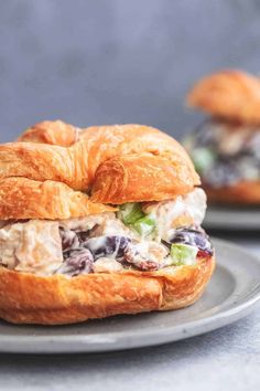 a croissant sandwich with chicken salad on it is sitting on a gray plate