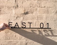 a hand is pointing to the word east 01 on a concrete wall with a shadow