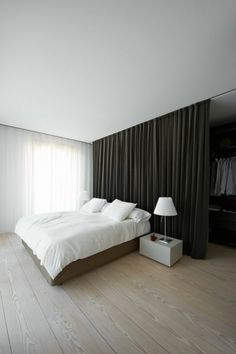 a large white bed sitting in a bedroom next to a tall window with curtains on it