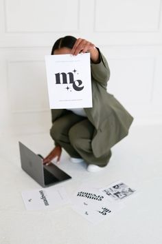 a woman kneeling on the ground holding up a sign with her hand and laptop in front of her