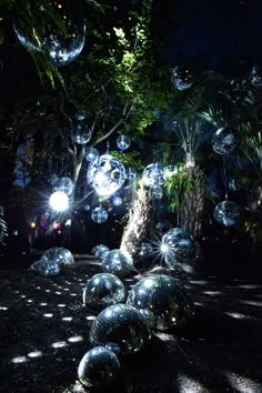 many shiny balls are floating in the air next to a tree and some trees with lights on them