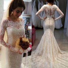 a woman wearing a wedding dress with long sleeves and lace on the back, standing in front of a mirror