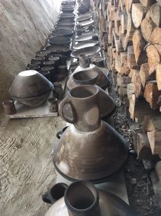 pottery is lined up on the floor next to stacks of wooden planks and logs