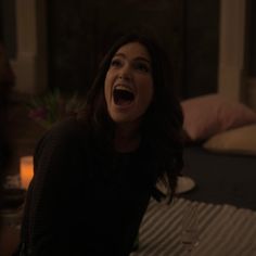 a woman sitting on top of a bed with her mouth open and wine glasses in front of her