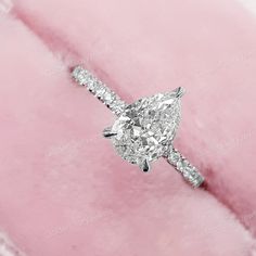 an oval shaped diamond ring sitting on top of a pink velvet bag