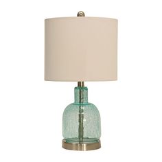 a green glass table lamp with a white shade on the base and a beige linen lampshade