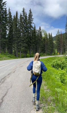 a woman is walking down the road with her back turned to the camera while carrying a backpack