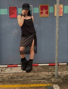 a woman is standing on the sidewalk talking on her cell phone while wearing a black hat