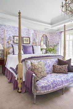 a bedroom with purple and white bedding, chandelier, couch and mirror on the wall