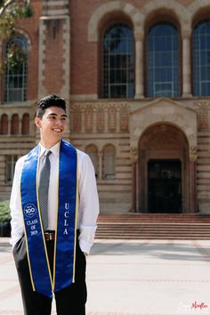 a man wearing a blue and yellow graduation stole standing in front of a large building