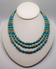 "Vintage Textured Gold Tone Beads and Aqua Blue Faux Turquoise Faceted Beads Triple Strand Necklace. The necklace is marked Trifari with the crown over the T and also has the metal Crown over T hang tag. The Set was part of their \"Electra\" collection circa 1962. The necklace has a hook closure for adjustability. The small gold tone bead spacers have some discoloring from age closer to the back of the necklace as well as the strand connectors and hook. Be sure to check out all the pictures for Turquoise Beaded Necklaces For Costume Jewelry, Turquoise Beaded Necklace For Costume Jewelry, Costume Jewelry Turquoise Beaded Necklace, Turquoise Beaded Costume Jewelry Necklace, Turquoise Costume Jewelry Beaded Necklace, Vintage Turquoise Jewelry With Colorful Beads, Blue Beaded Turquoise Costume Jewelry Necklace, Turquoise Beaded Necklace With Gold Round Beads, Vintage Turquoise Beaded Necklaces With Round Beads