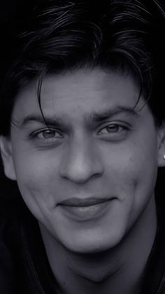 a young man smiling at the camera with his hair pulled back and wearing a black jacket