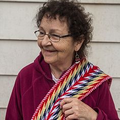 an older woman wearing glasses and holding a colorful knitted scarf in front of a house