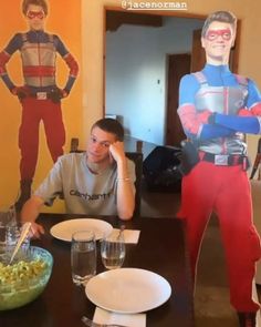 a man sitting at a table in front of two paper cutouts of superheros