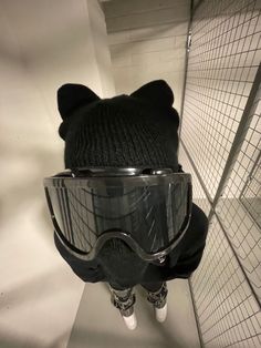 a teddy bear wearing a knitted hat and goggles in a room with wire mesh walls