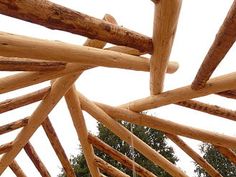 the inside of a wooden structure that is made out of wood sticks and logs, with trees in the background