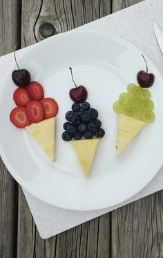 a white plate topped with slices of fruit and cheese covered in grapes, strawberries, cherries, and blueberries