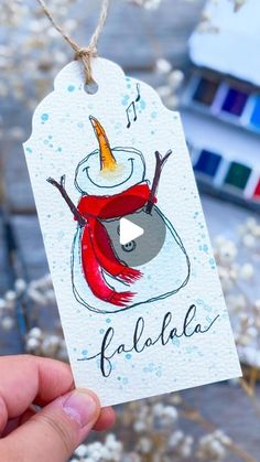 a hand holding up a tag with an image of a snowman in the background