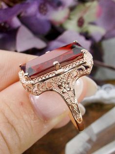 Garnet Cubic Zirconia (CZ) Rose Gold over Sterling Silver Ring 1915 Design#D232 This is a lovely antique Edwardian era inspired filigree ring. This gorgeous ring is set with a stunning garnet cubic zirconia (CZ) gem and overlaid with rose gold plating. The vibrant gemstone is 18mm x 9mm. The ring sits 21mm north-south and 12mm east-west on the finger. The inside of the band is marked 925 for sterling silver. The band and setting have intricate filigree, with hints of floral influence across it. Vintage Ruby Ring With Filigree For Wedding, Victorian Rose Gold Ruby Ring, 14k Gold Filigree Ruby Ring Gift, 14k Gold Ruby Ring With Filigree For Gift, Vintage Gold Ruby Ring With Filigree, Victorian Ruby Ring With Filigree For Wedding, Antique Style Ruby Ring With Intricate Design For Wedding, Victorian Ruby Ring With Intricate Design For Formal Events, Victorian Ruby Ring With Rose Cut Diamonds For Wedding