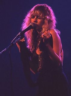 a woman standing in front of a microphone with her hand on the mic and singing