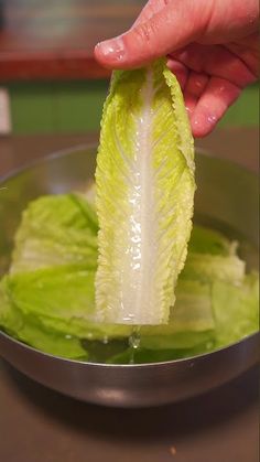 a hand is holding a piece of lettuce in a metal bowl on a table