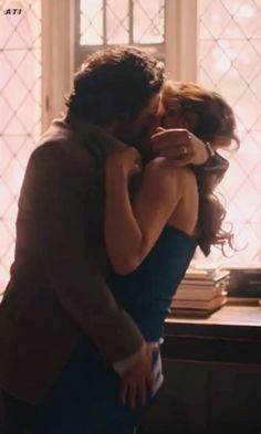 a man and woman embracing each other in front of a window